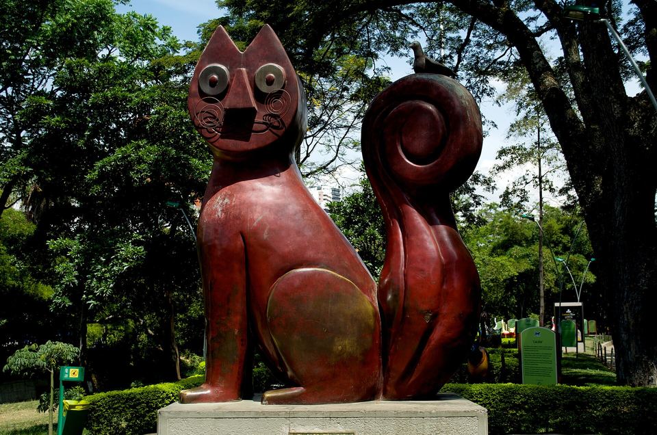 Escultura roja del Gato del Río, de Hernando Tejada, entre los árboles junto al río Cali